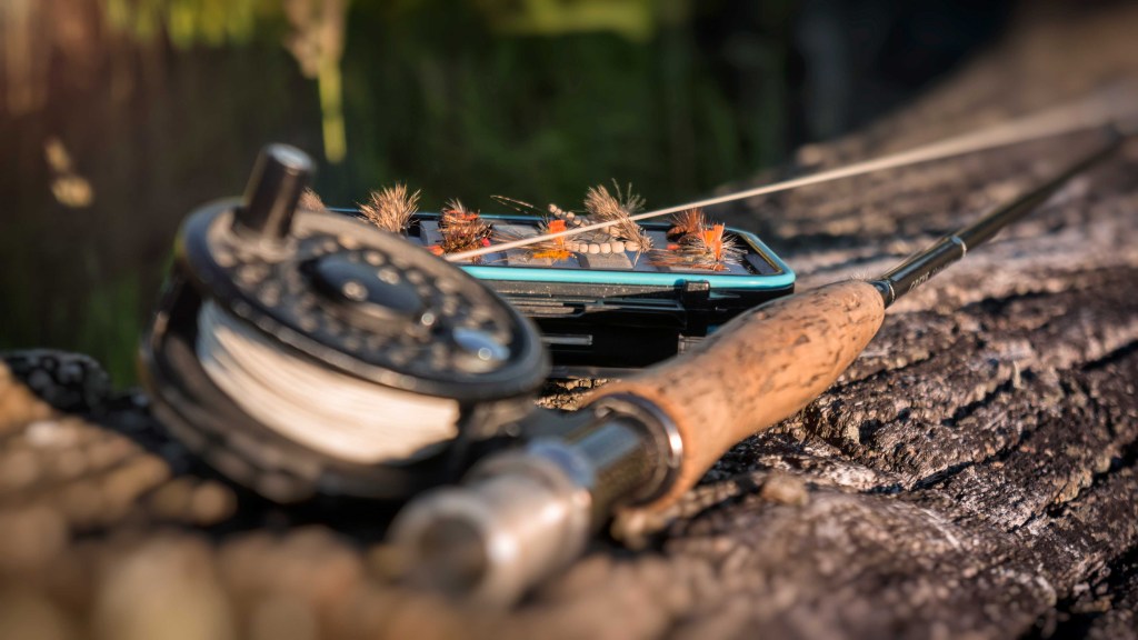 fly rod with dry fly box on a log